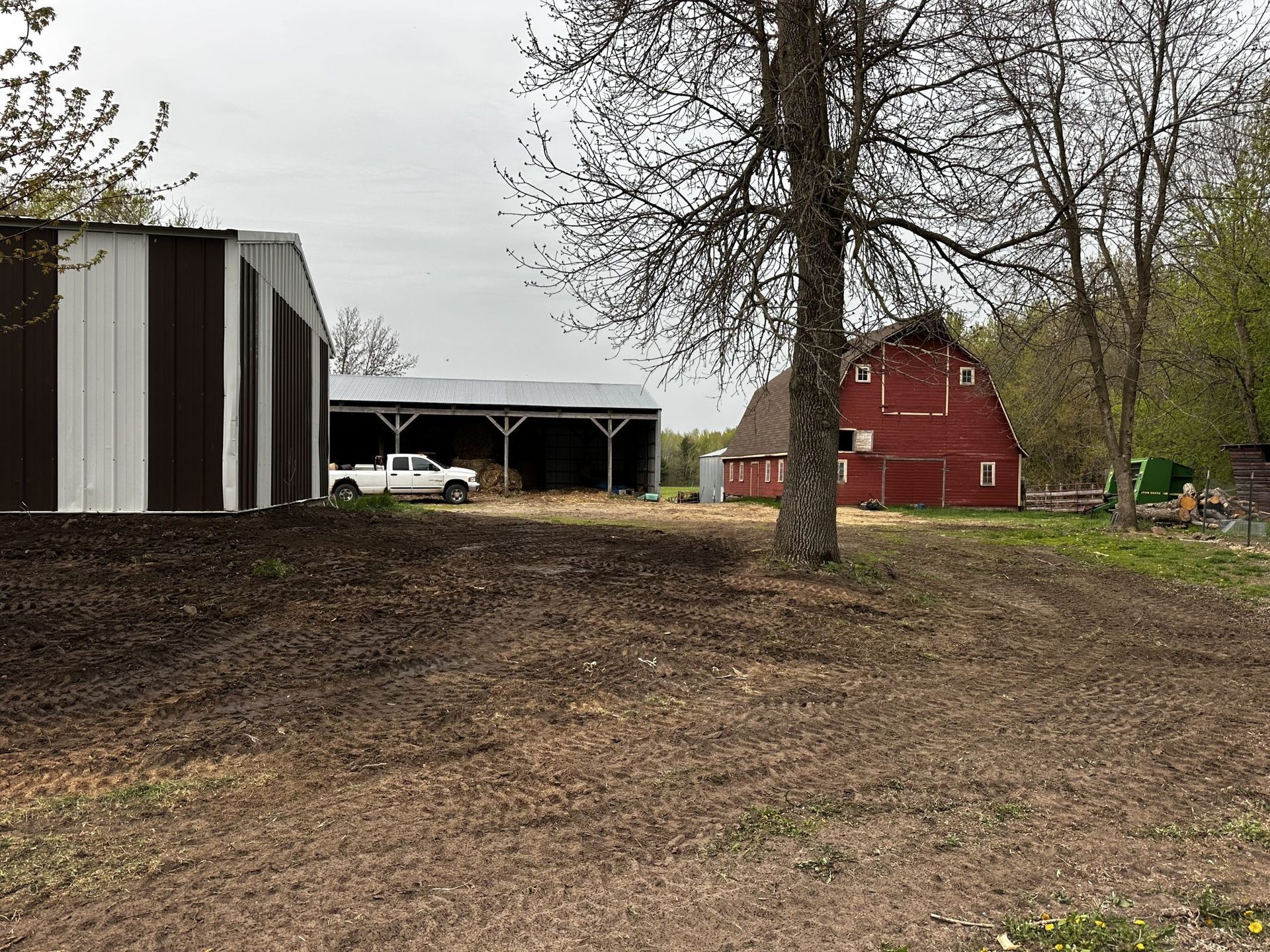 Rural farmyard with a red barn, striped shed, and leafless trees on a cloudy day