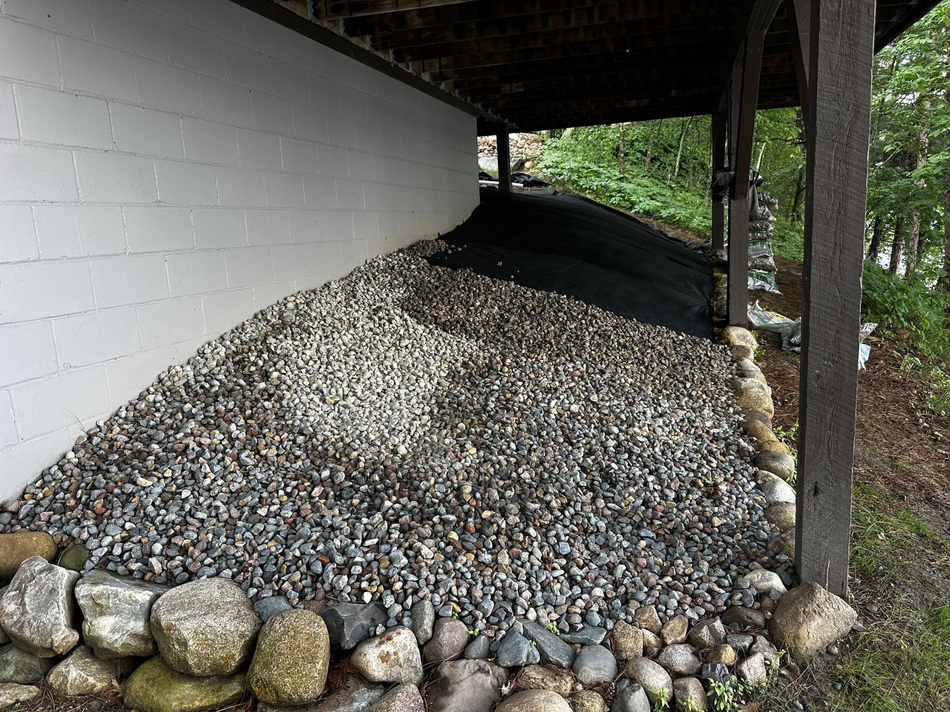 Gravel slope under a building overhang beside a white wall and stone border