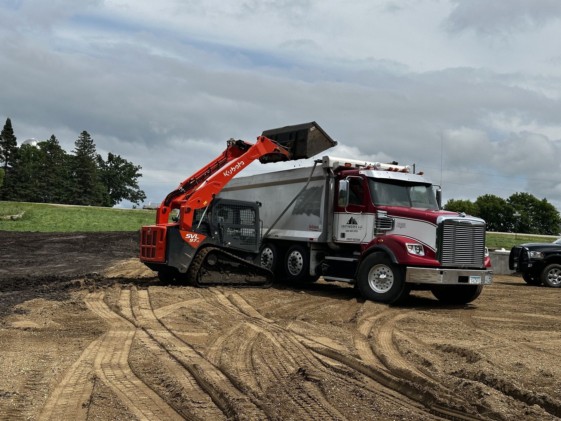Red dump truck with raised bed in a dirt lot under cloudy skies