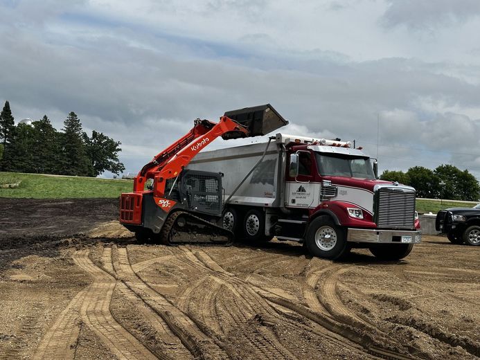 Red dump truck with raised bed in a dirt lot under cloudy skies