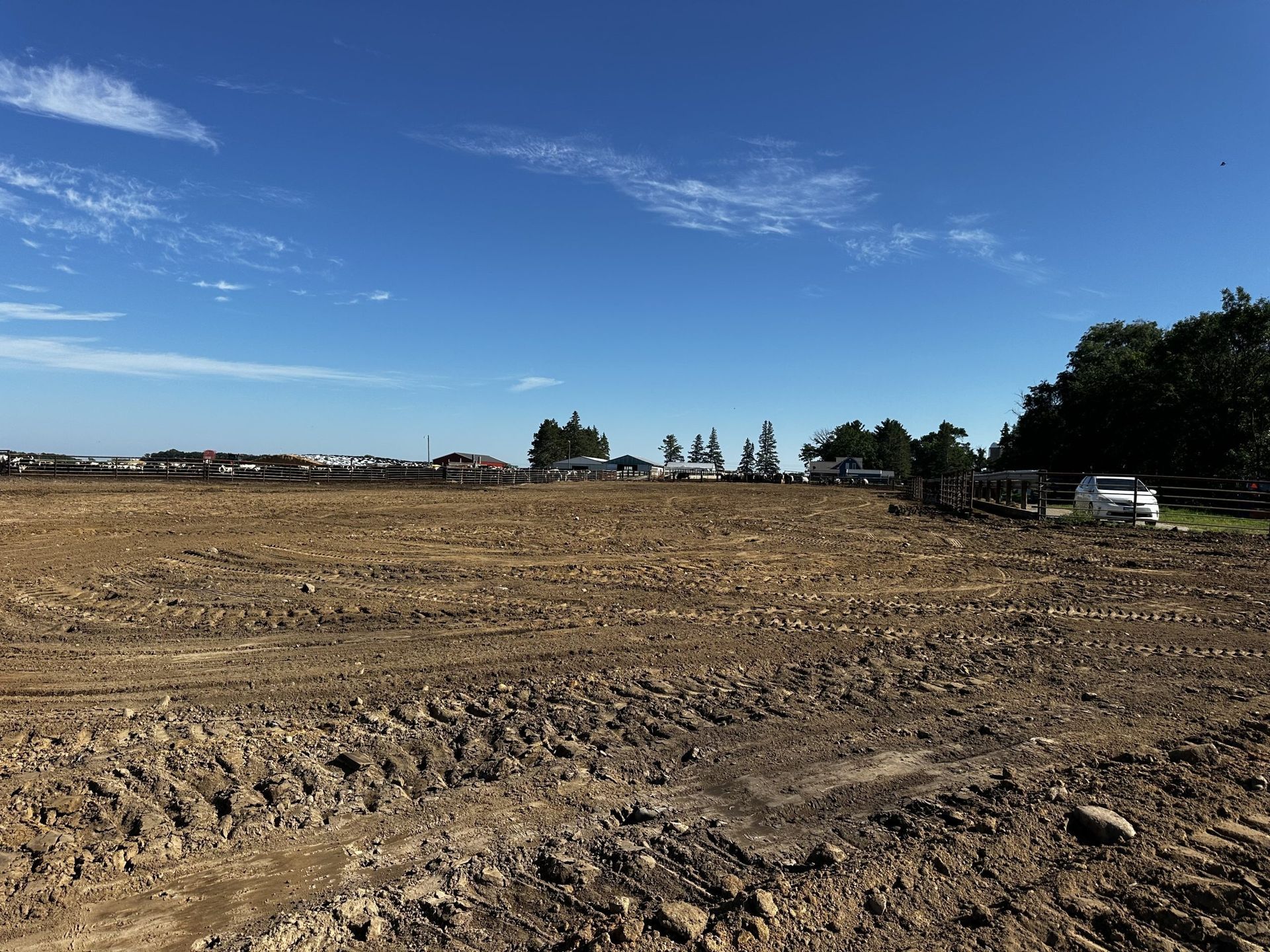 Plowed dirt field under a bright blue sky, with trees and a white truck in the distance