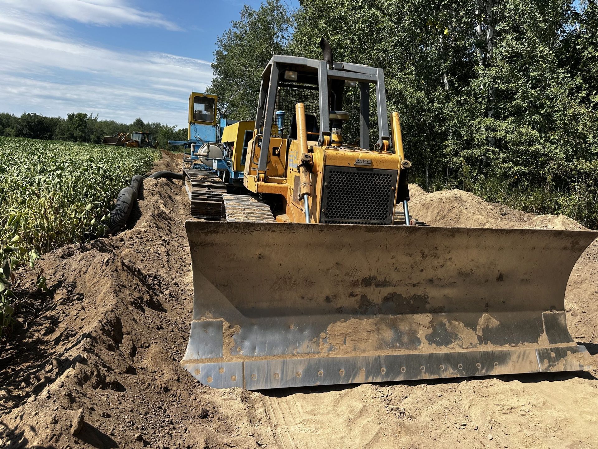 Yellow bulldozer leveling a dirt road beside a field and trees