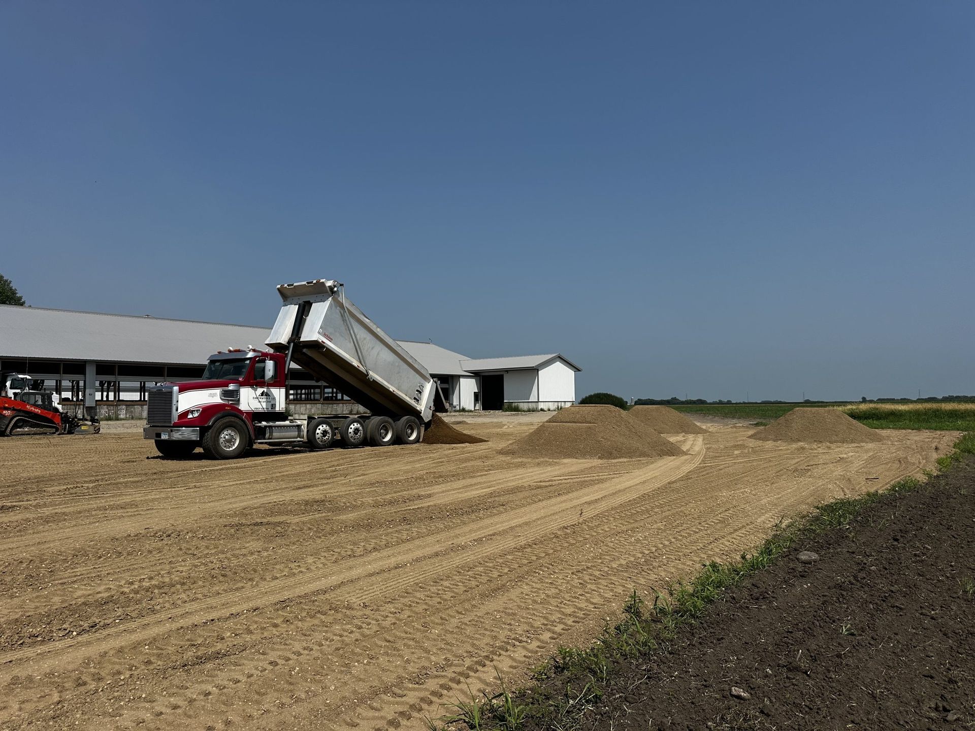 Dump truck unloading gravel on a dirt road at a construction site under a clear blue sky