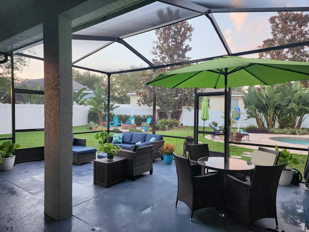 Patio with outdoor furniture, green umbrella, and screen enclosure overlooking a backyard with a pool.