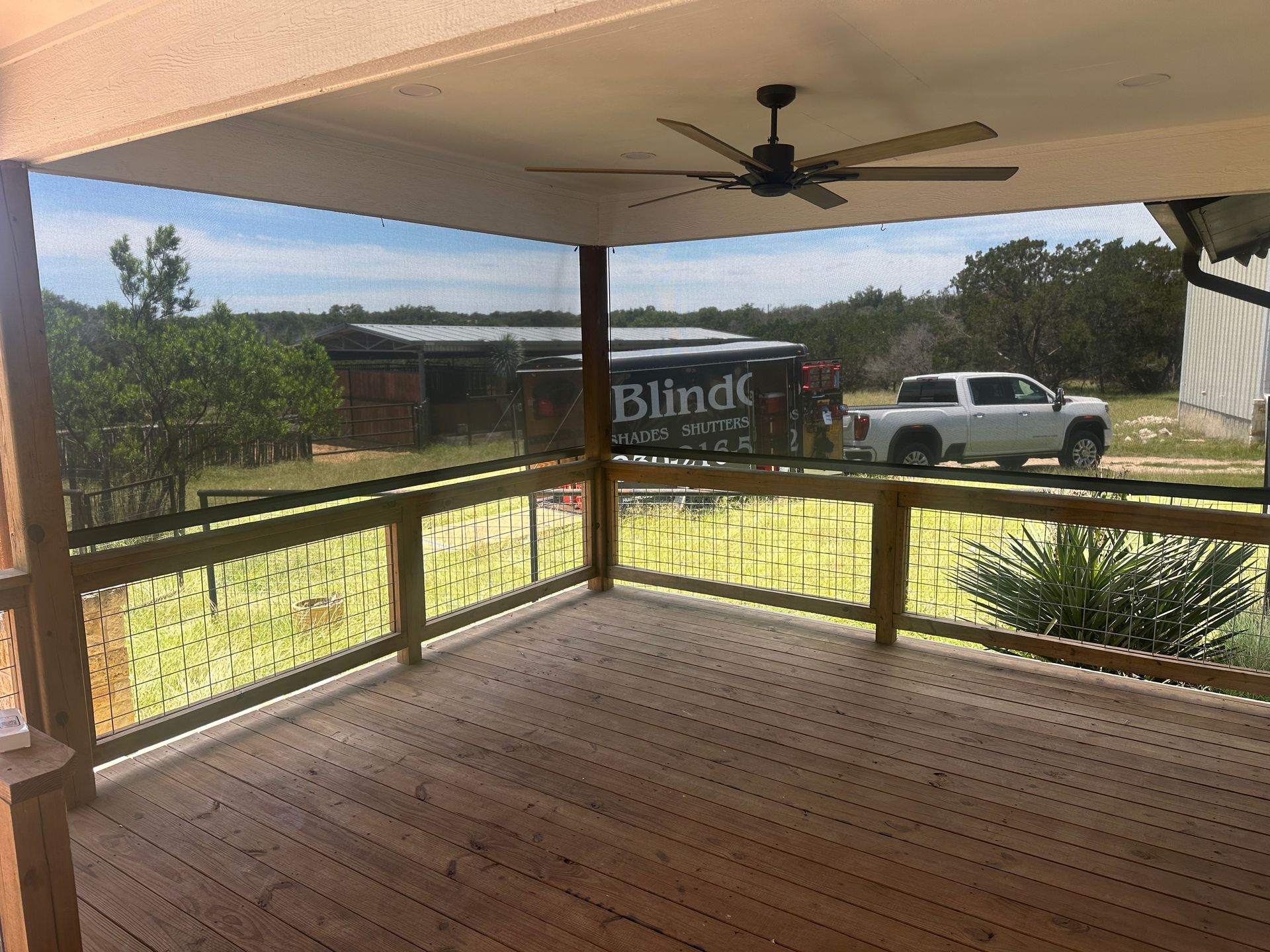 Covered wooden porch with ceiling fan, railing, yard, and white truck in the background.