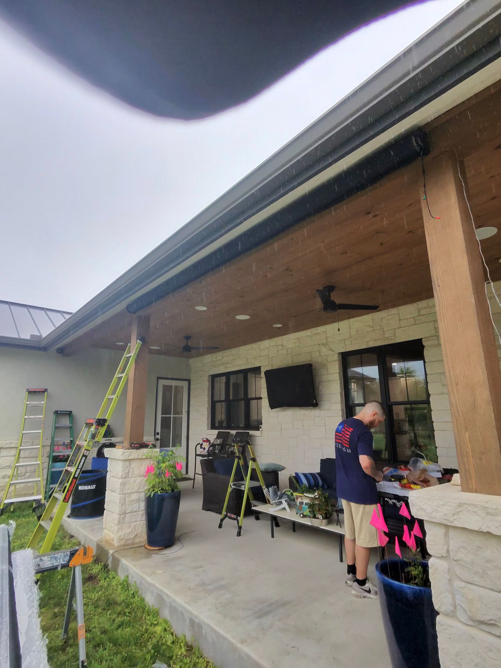 Porch under construction with ladder, tools, and a person tending a child near the house