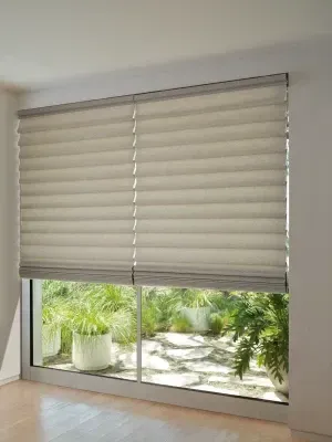 Closed beige window blinds with a view of green plants and sunlight outside