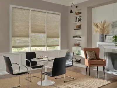 Modern dining room with round glass table, black chairs, tan accent chair, and bright windows with blinds