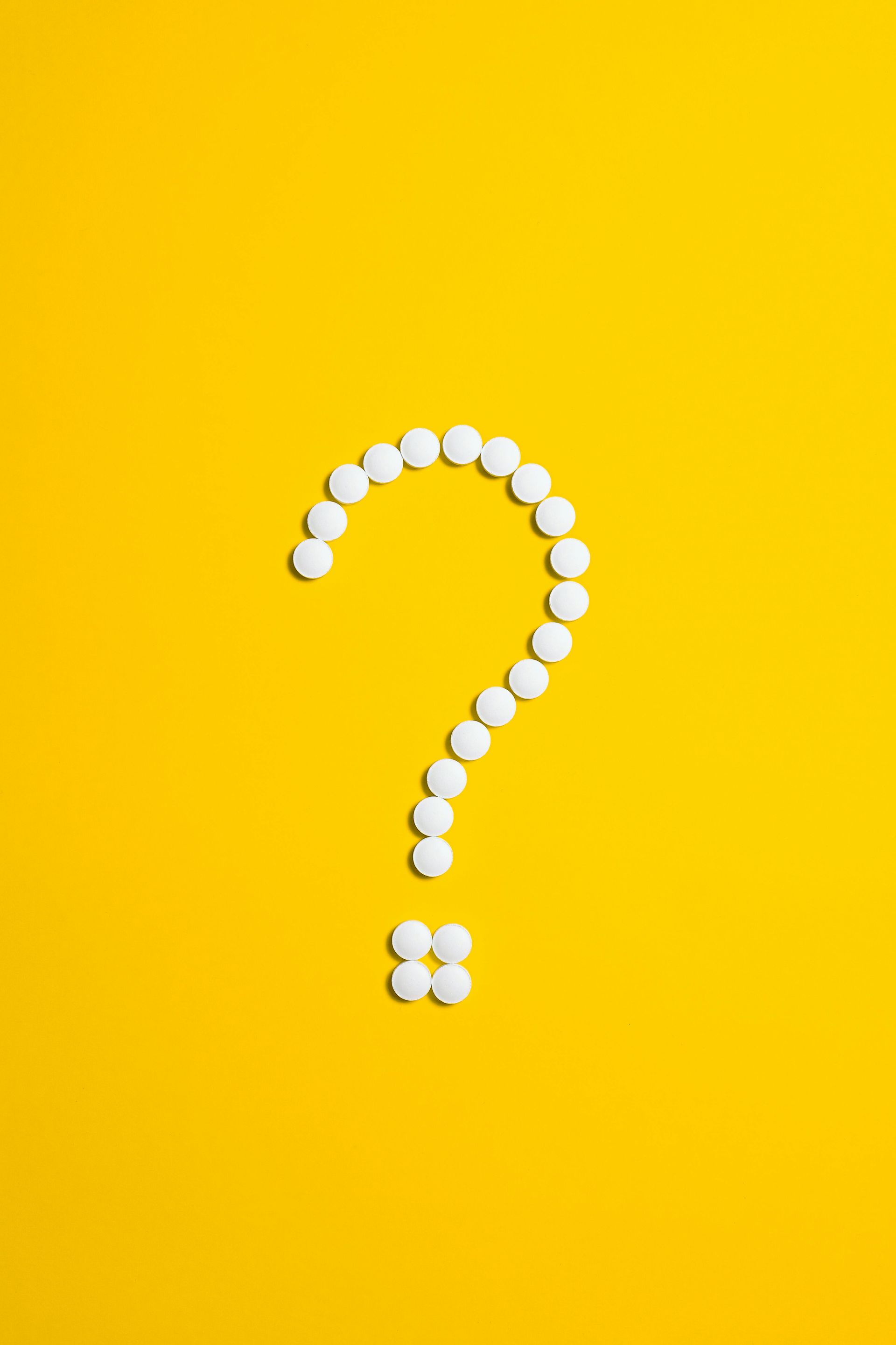 A question mark made of white pills on a yellow background.