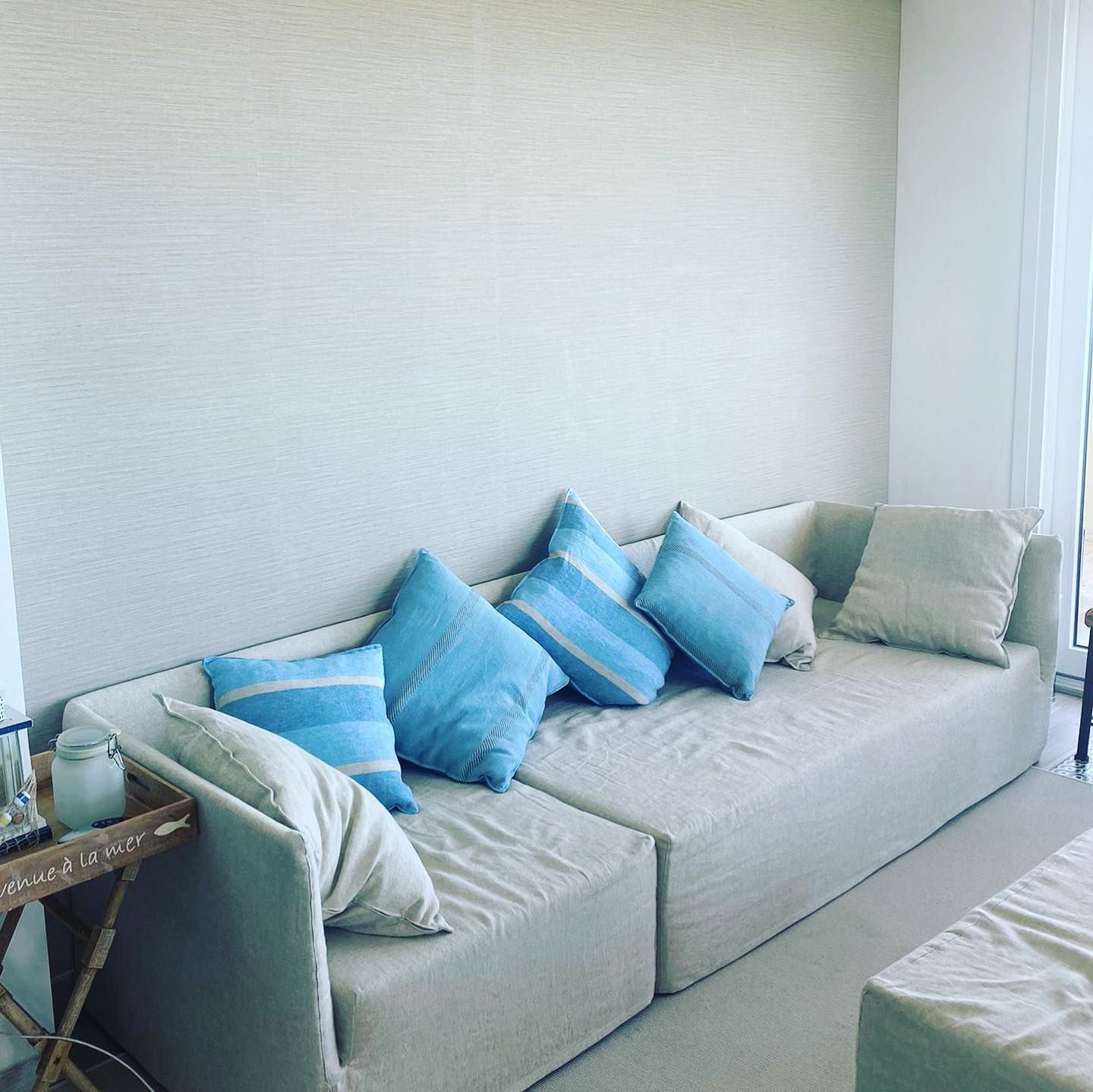 Divano modulare beige con cuscini blu e beige contro una parete chiara.