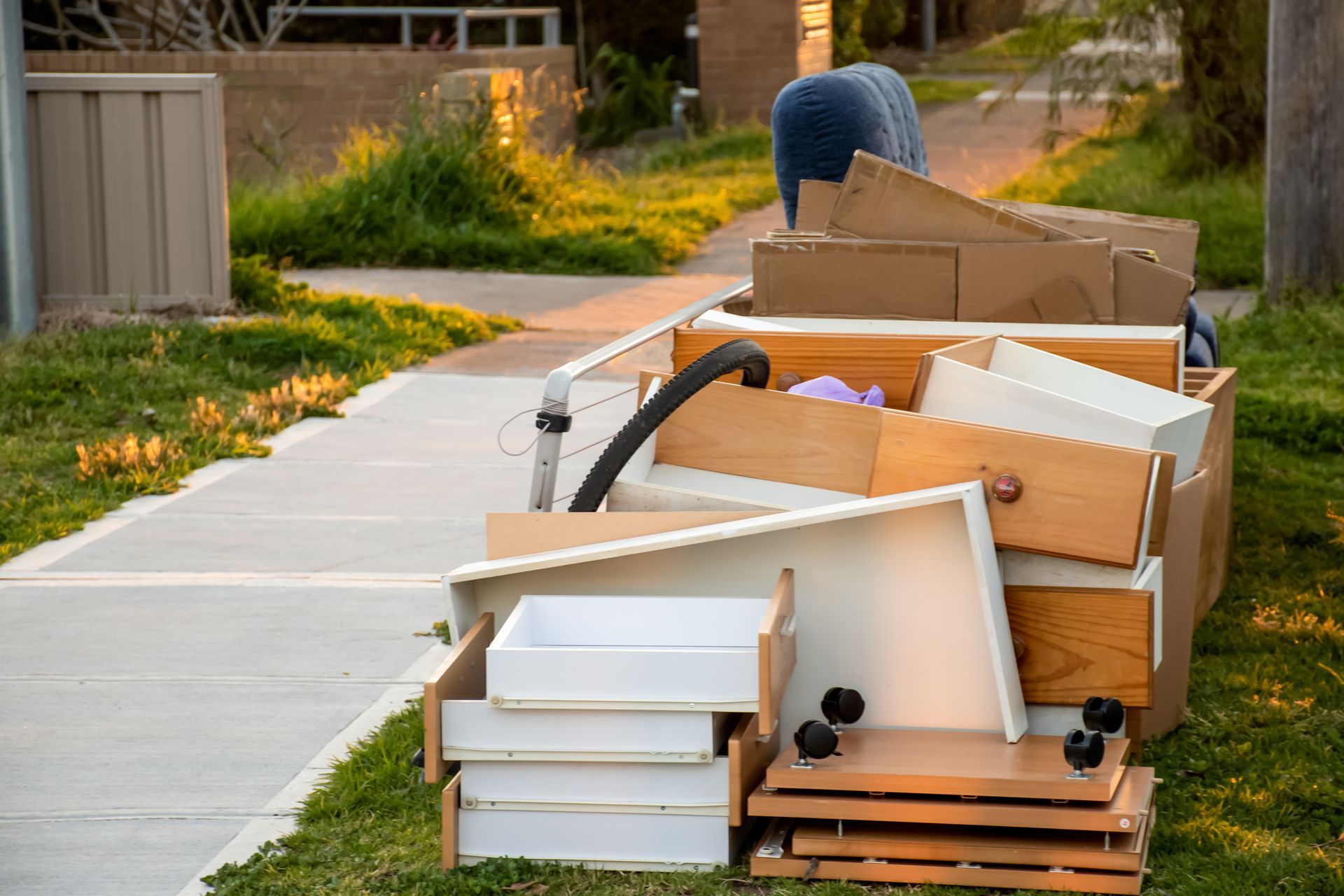 Heap of discarded furniture on a sidewalk, including drawers, boxes, and a vacuum cleaner.