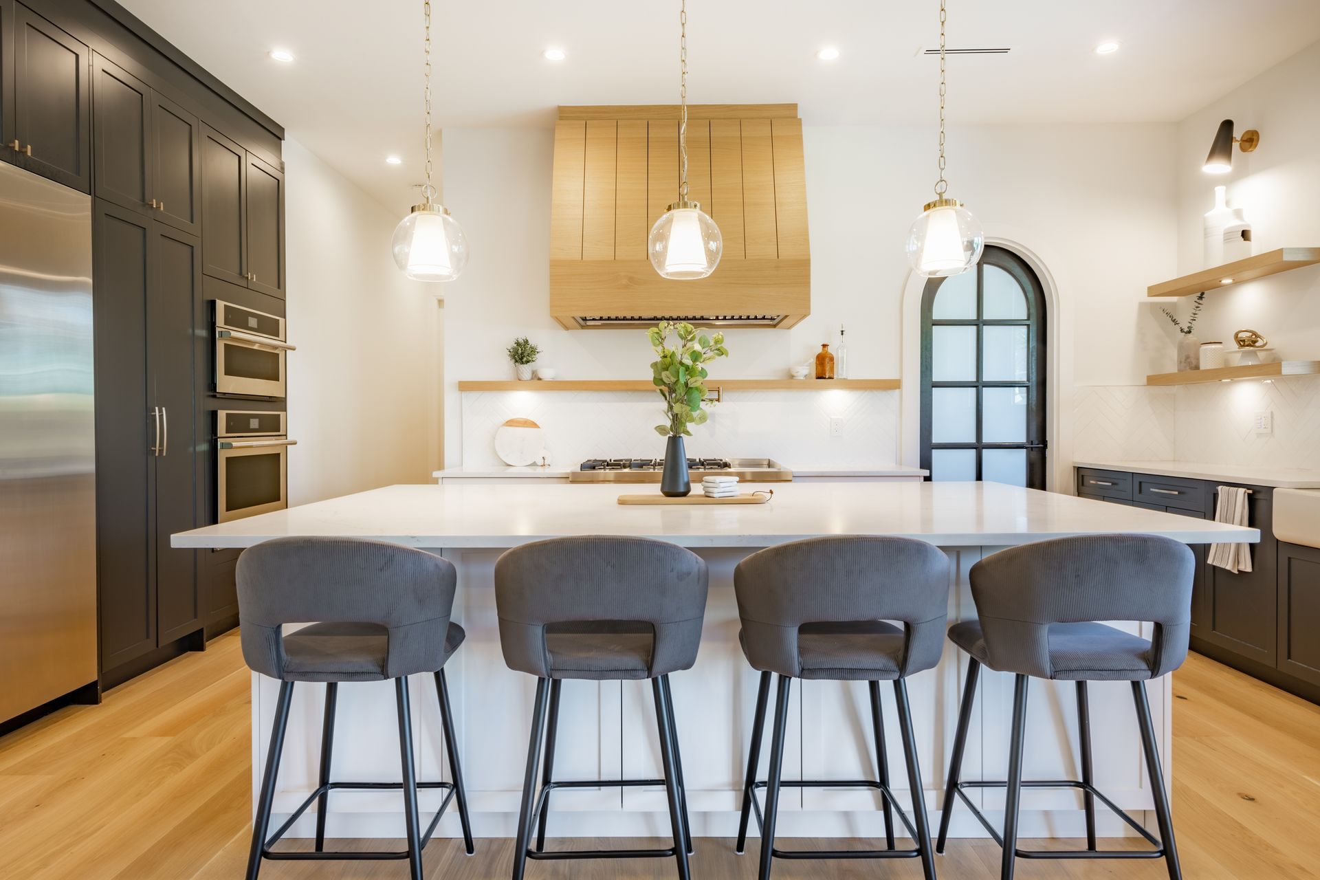 Modern kitchen with a large island, four bar stools, and wooden range hood.