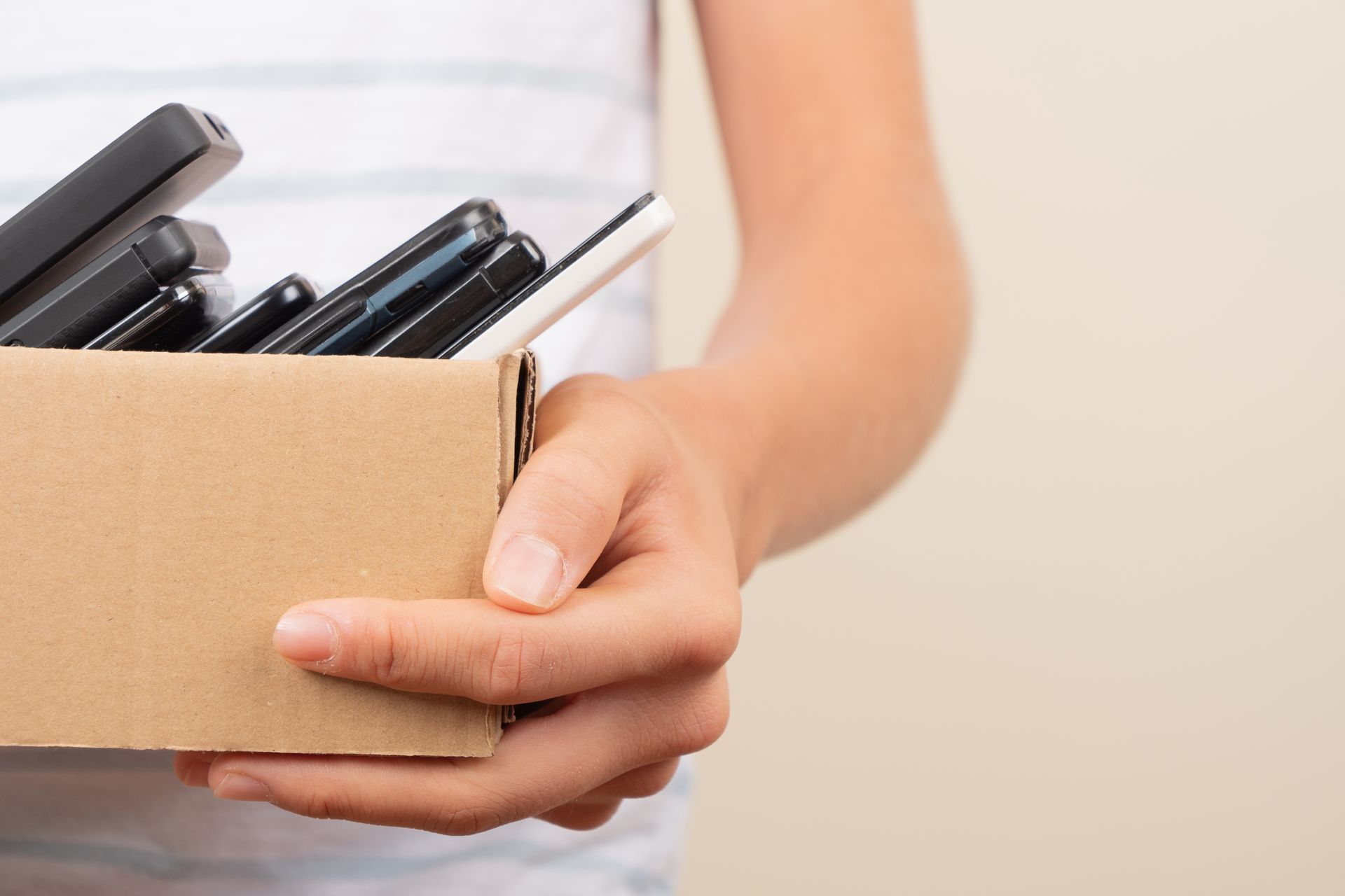 Person holding a cardboard box filled with smartphones.