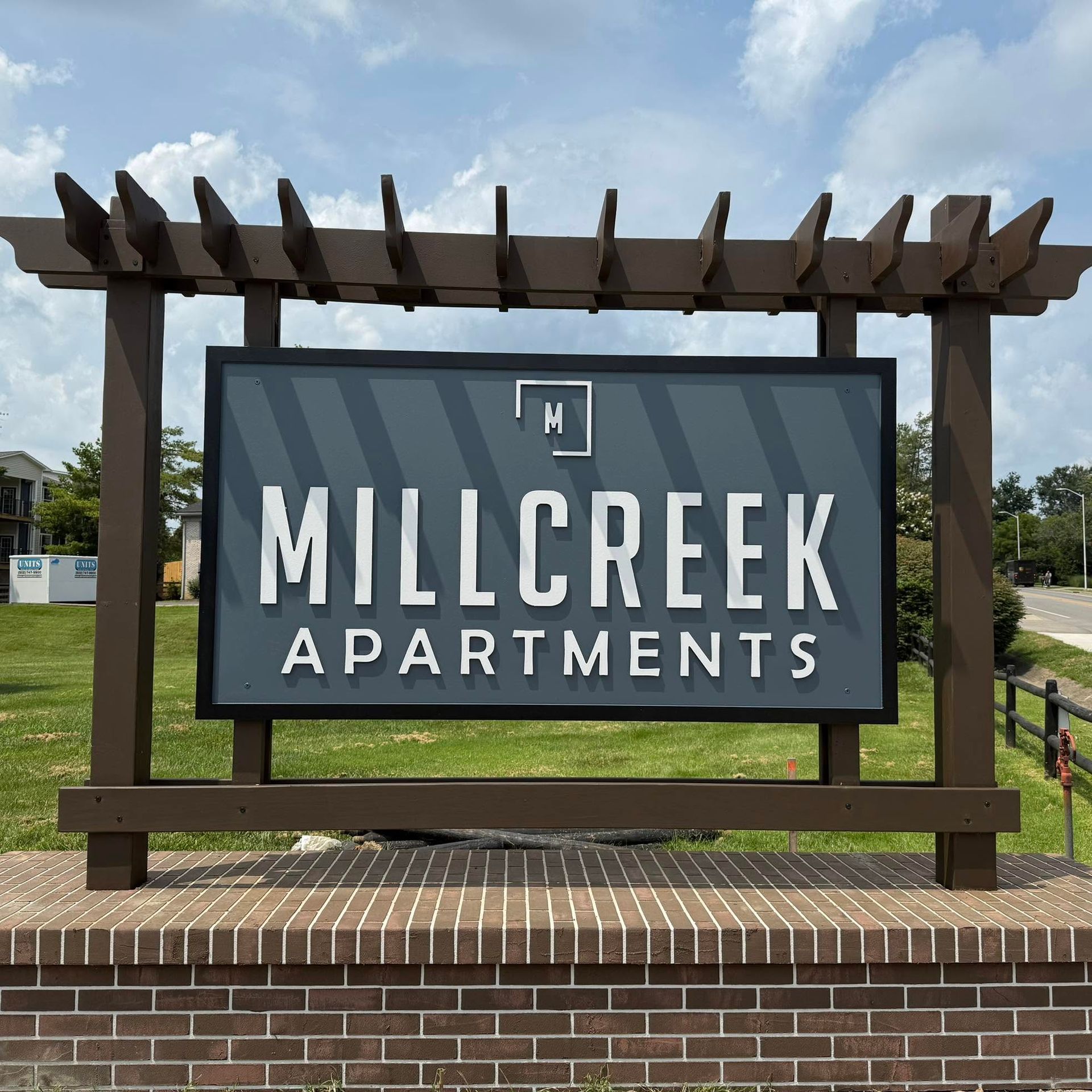Millcreek Apartments entrance sign with modern wooden pergola frame and brick base in front of the c