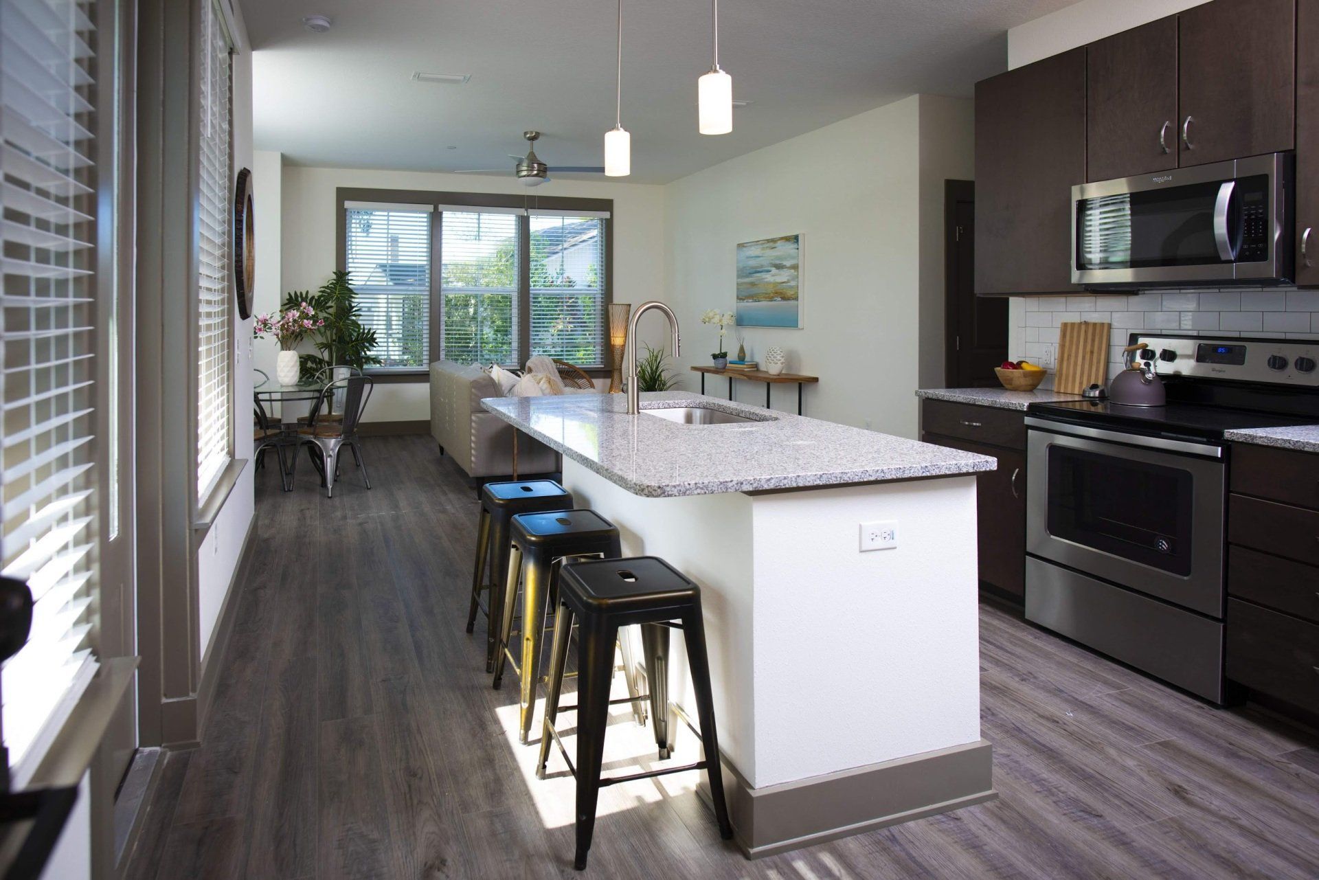 Photo showing a kitchen, featuring an island and barstools, as well as the living room in the background