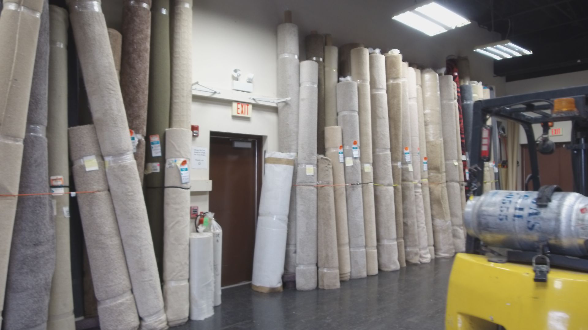 Rows of rolled carpets stacked in a warehouse aisle beside a forklift