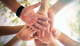 Stacked hands of several people joining together in a group huddle outdoors
