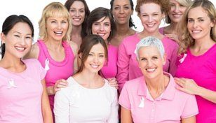 Group of smiling people in pink shirts posing together against a white background