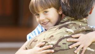 Smiling child in blue-and-white striped shirt hugging a person in camouflage uniform