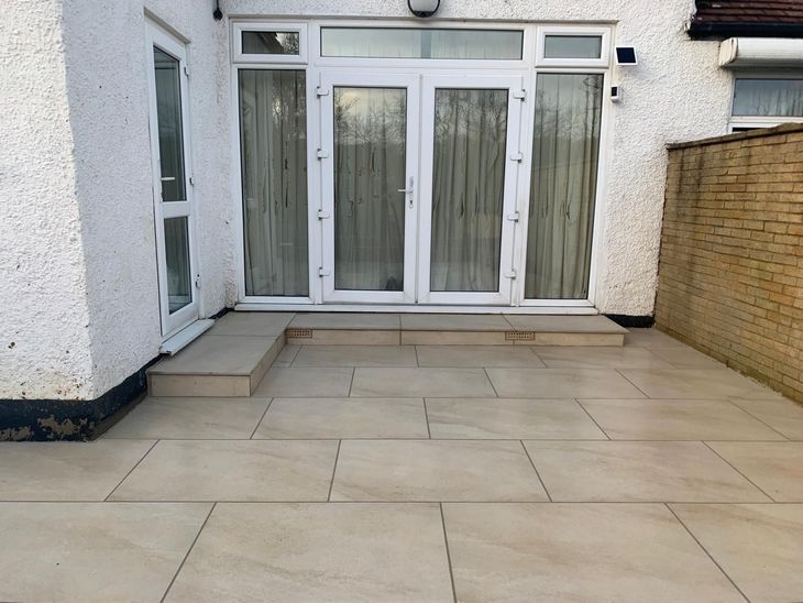 Patio with light beige rectangular pavers leading to a white door. A low step is present.