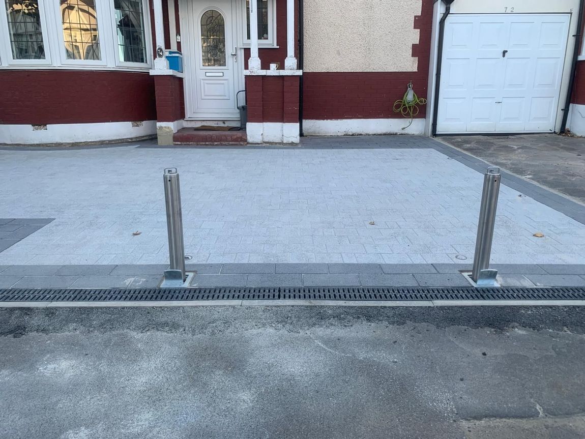 Residential driveway with two metal posts and a drainage grate in front of a garage and house entrance