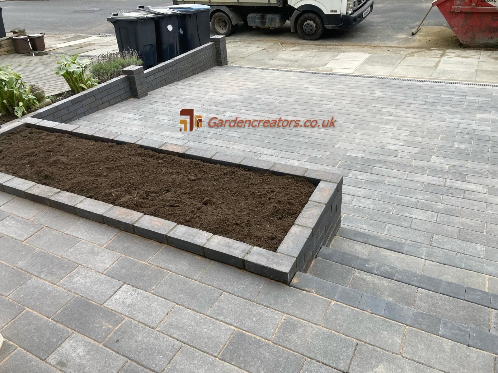 A large planter is sitting on top of a brick driveway.