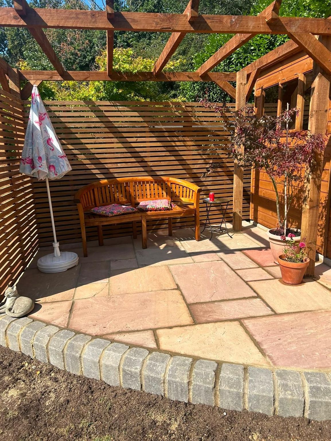 paving  garden patio with bench, umbrella, potted flowers, and pergola in sunlight