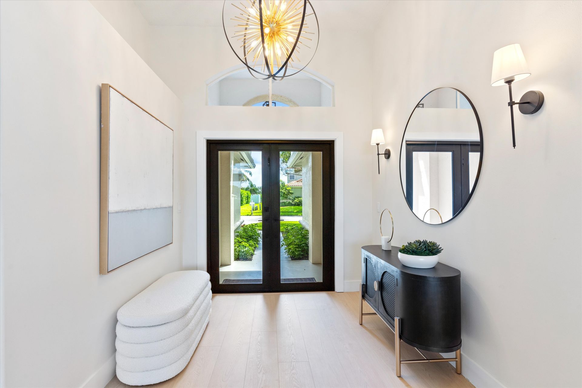 A hallway with a bench , mirrors , and a chandelier.
