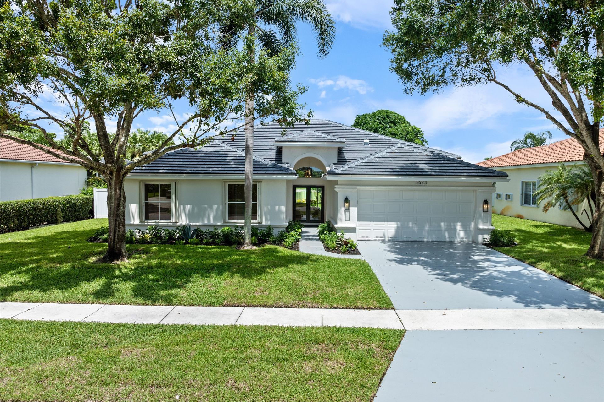 A white house with a black roof is for sale in a residential area.