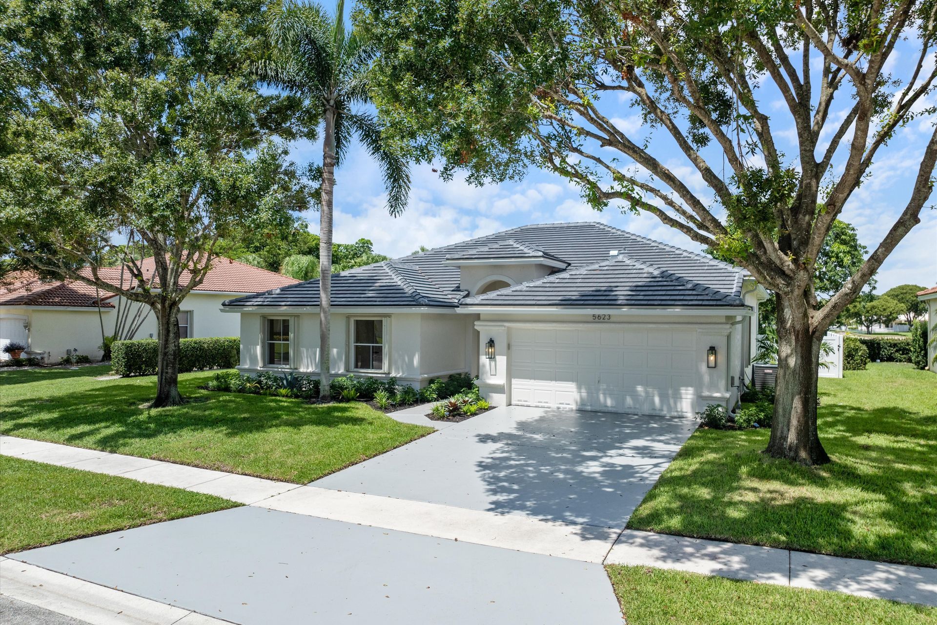 A white house with a garage and a tree in front of it.