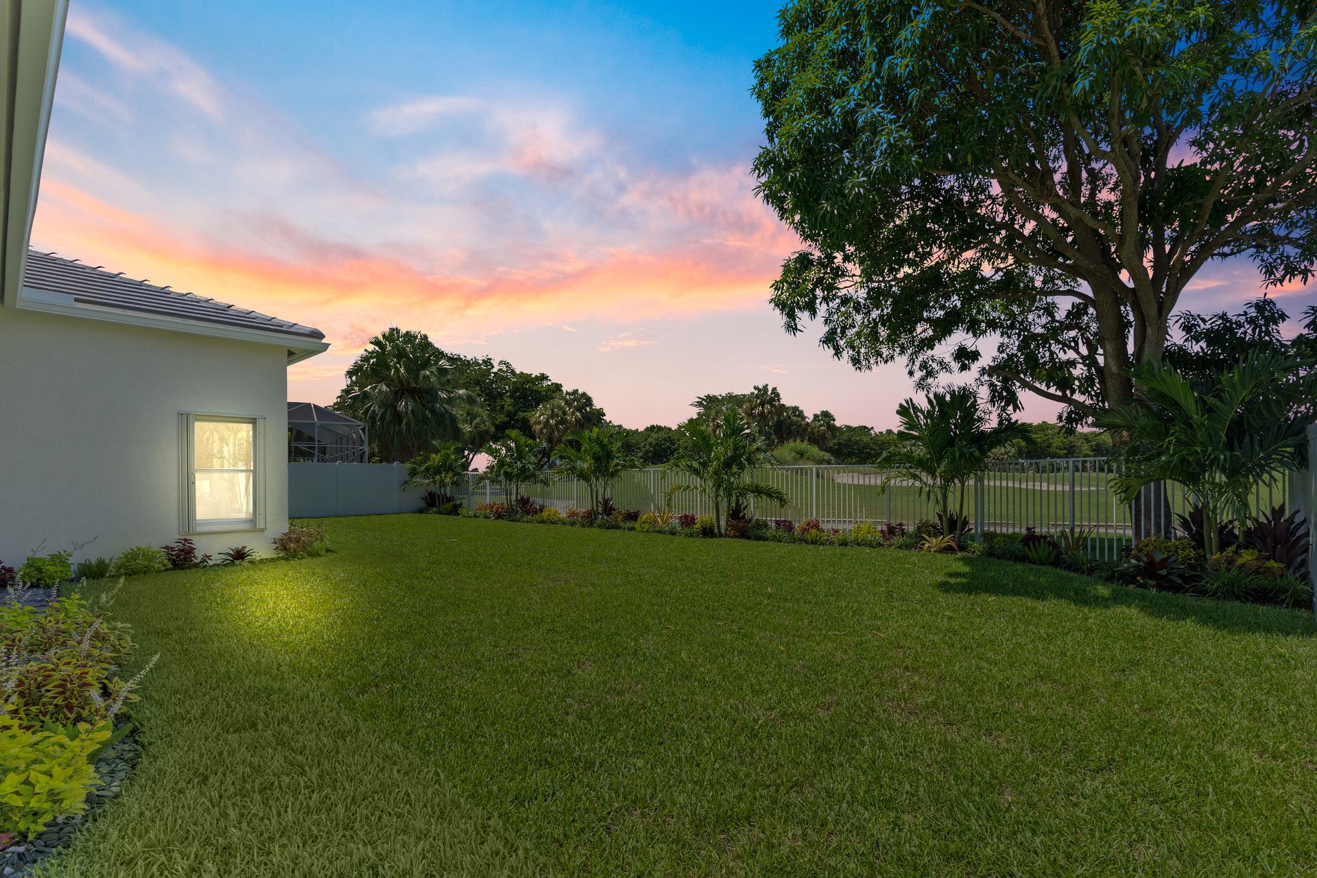 The backyard of a house with a large lawn and trees at sunset.