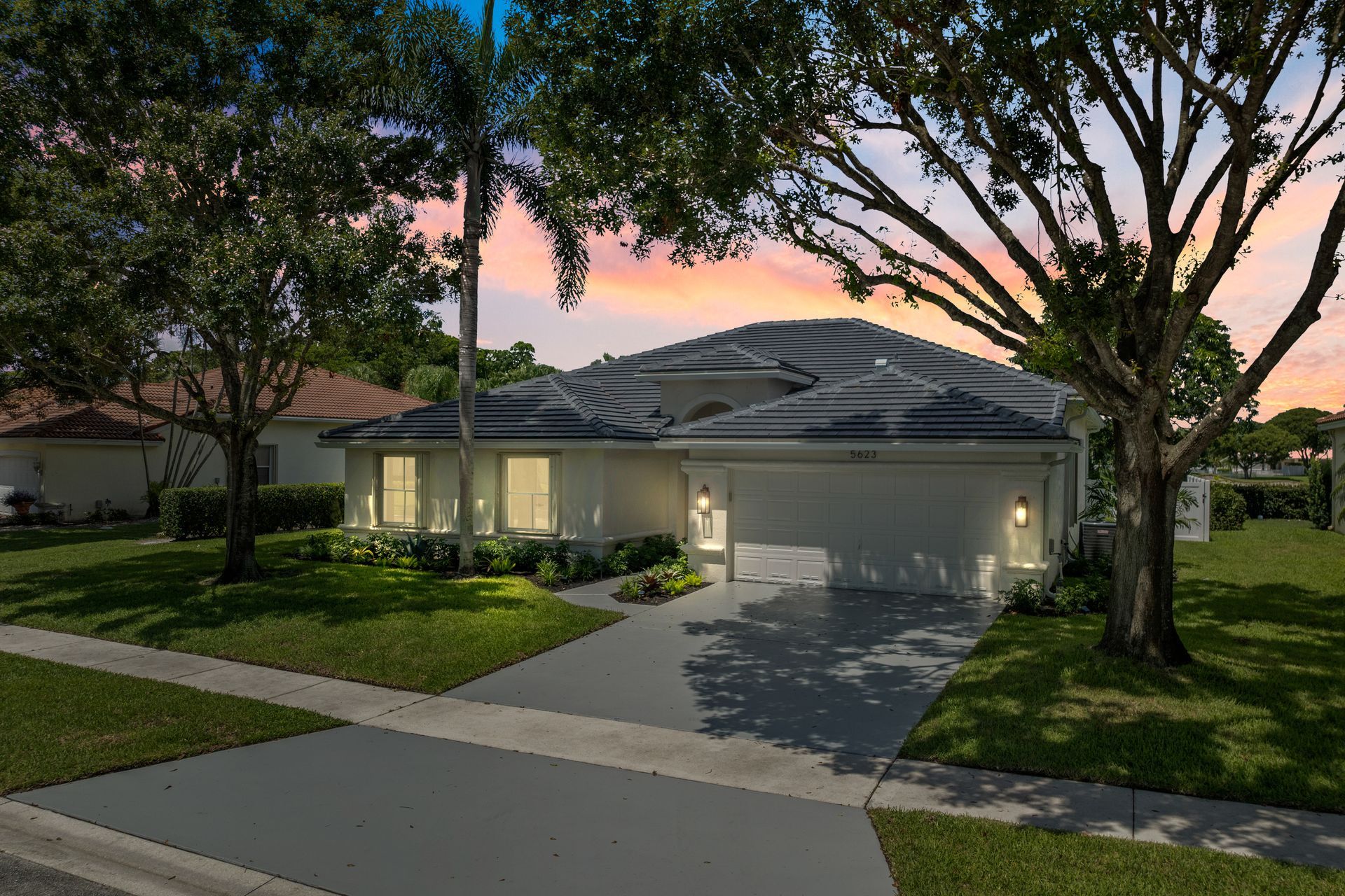 A white house with a garage and a tree in front of it.