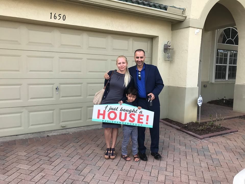 A family is standing in front of a house holding a sign that says `` i love my new house ''.