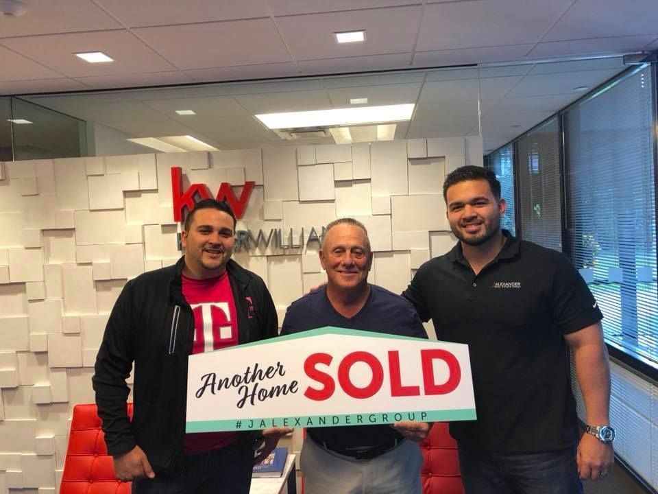 Three men are holding a sign that says another home sold