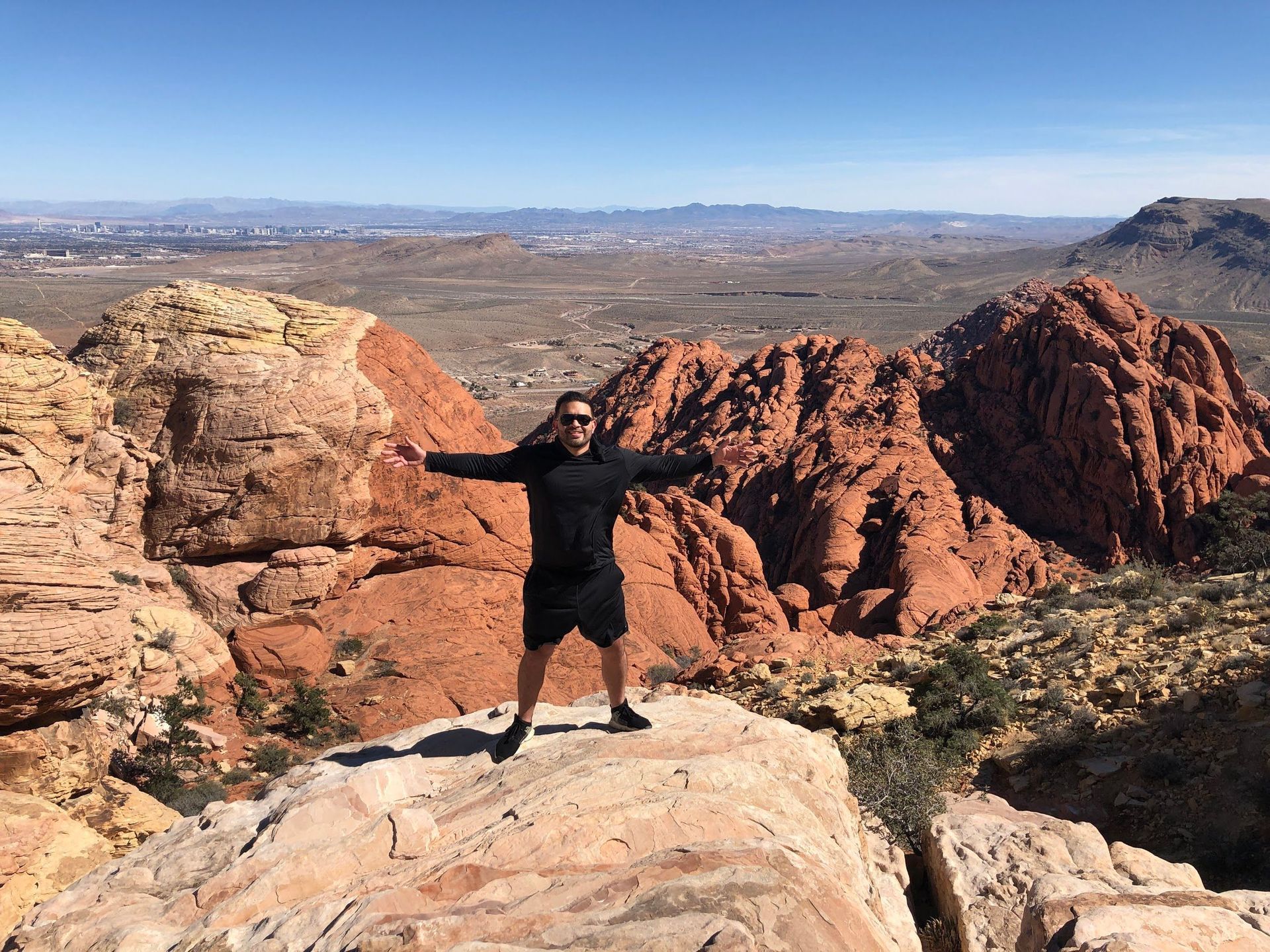 A man is standing on top of a rocky mountain with his arms outstretched.