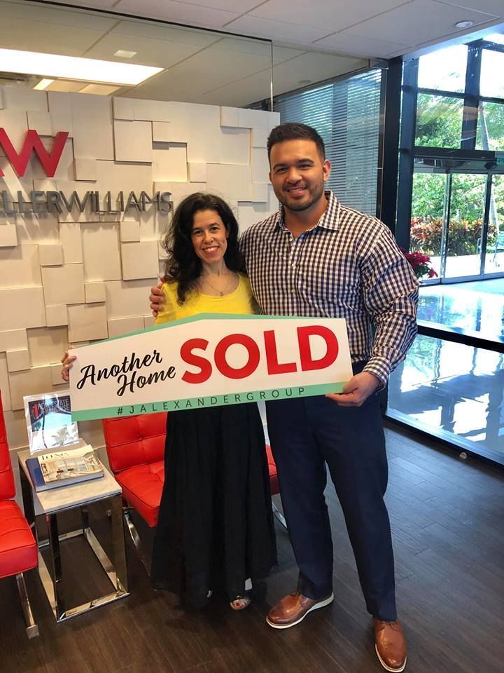 A man and a woman are holding a sold sign in a real estate office.