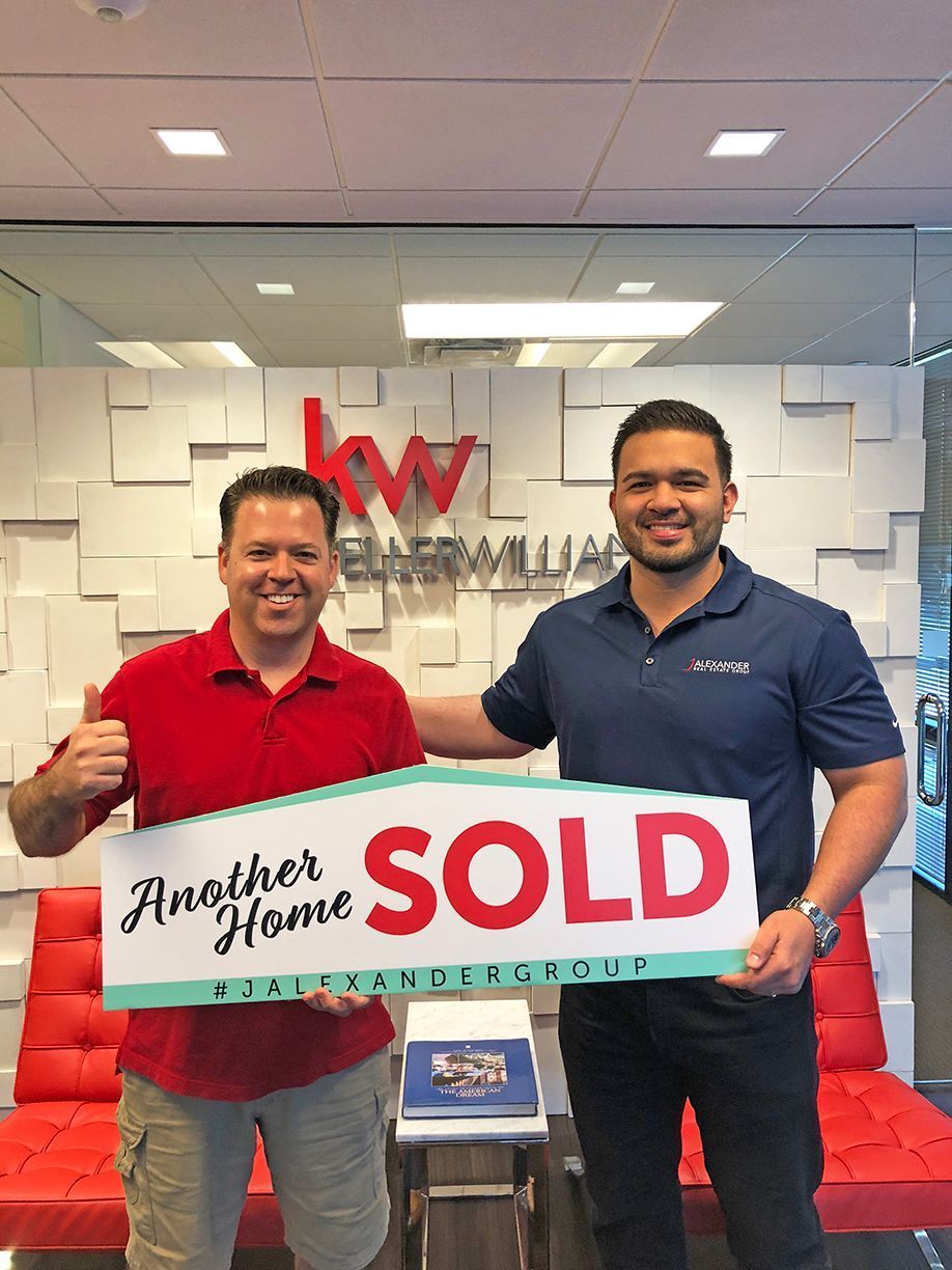 Two men are holding a sold sign in a real estate office.