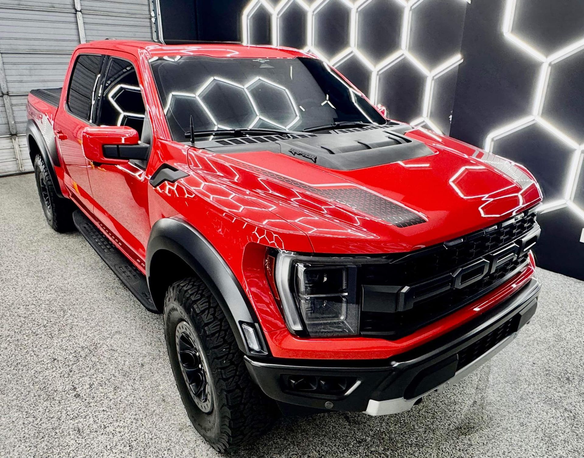 A red pickup truck is parked in front of a honeycomb wall.