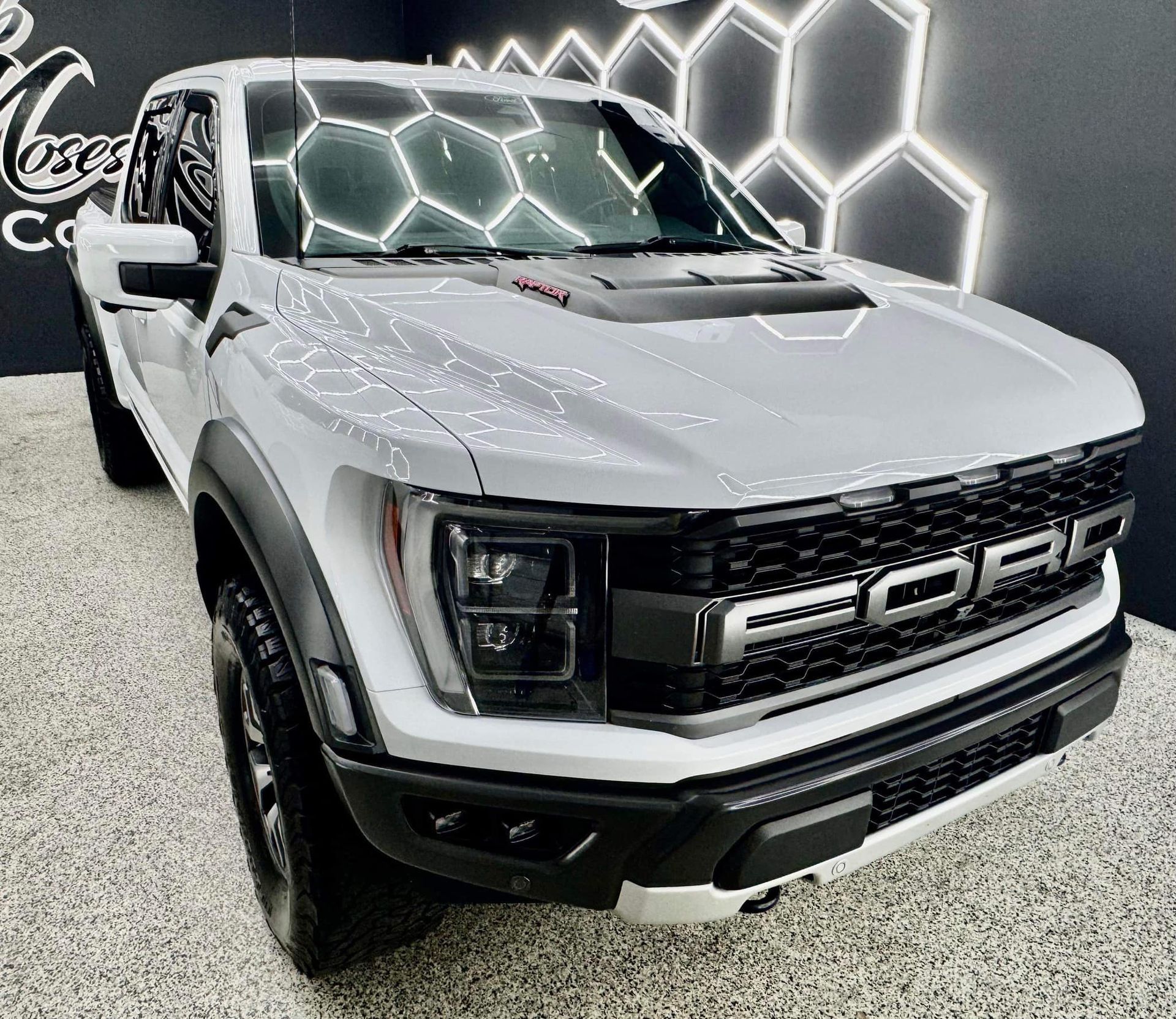 A white ford raptor truck is parked in a showroom.
