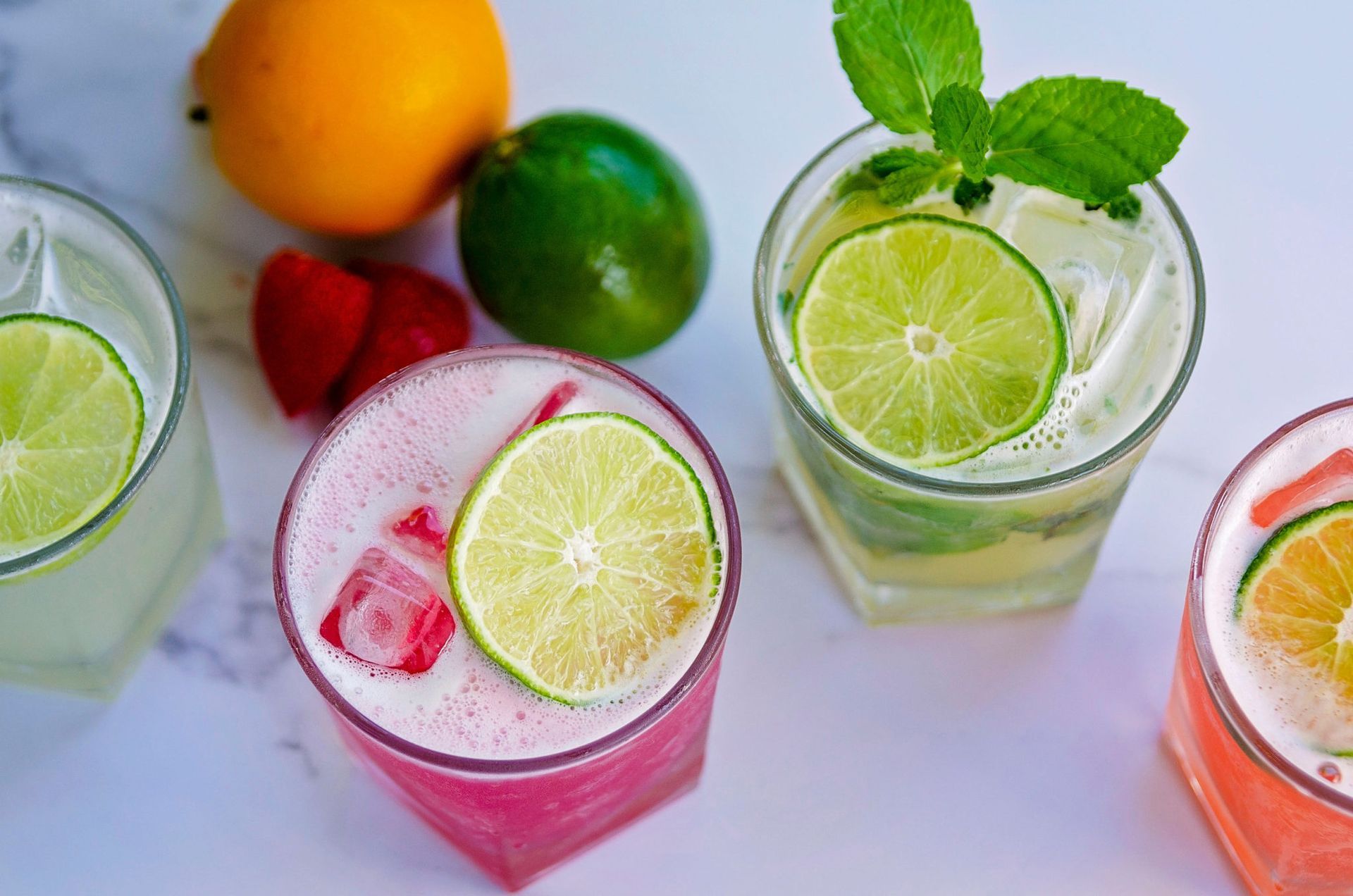 Three different colored drinks with lime slices and strawberries on a table.