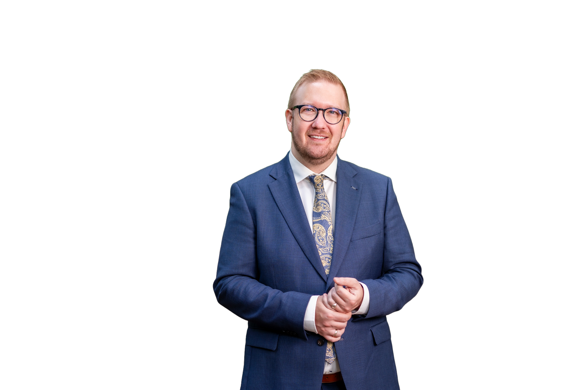 Een lachend persoon in een blauw, gestructureerd pak en een stropdas met patroon, met een bril op, staat tegen een effen witte achtergrond.
