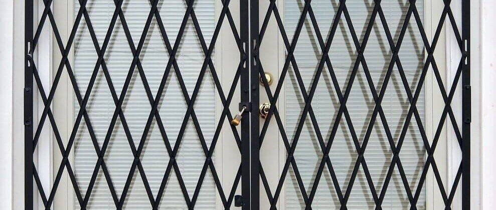 A close up of a metal gate on a door with blinds.