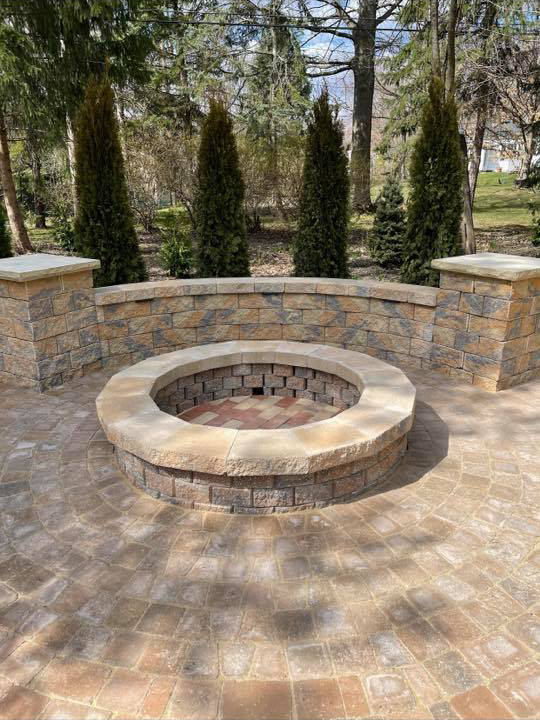 a fire pit is sitting on top of a brick patio surrounded by trees .