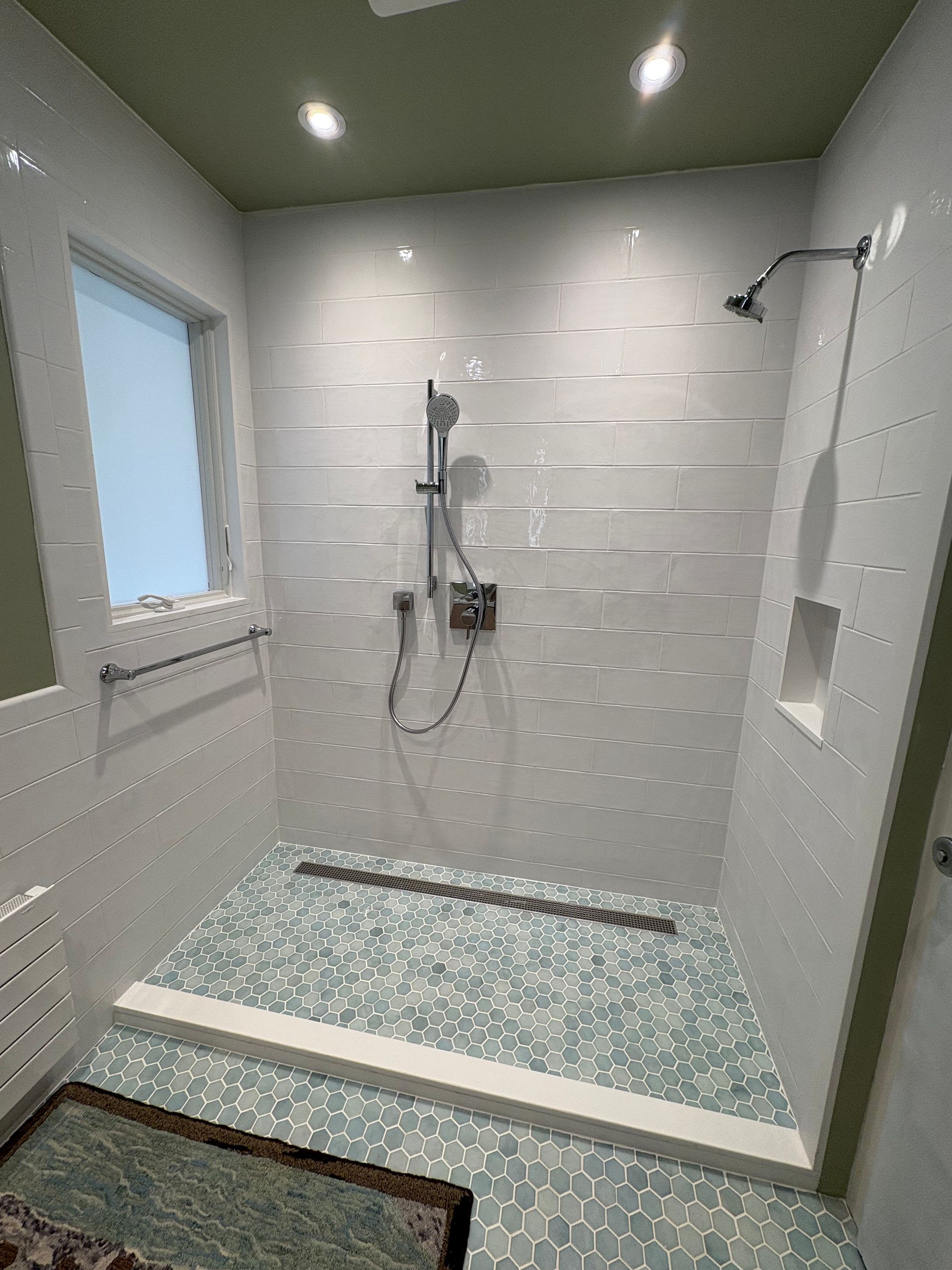 Accessible shower with handheld showerhead, grab bars, built-in bench, and pebble tile floor in a tiled bathroom