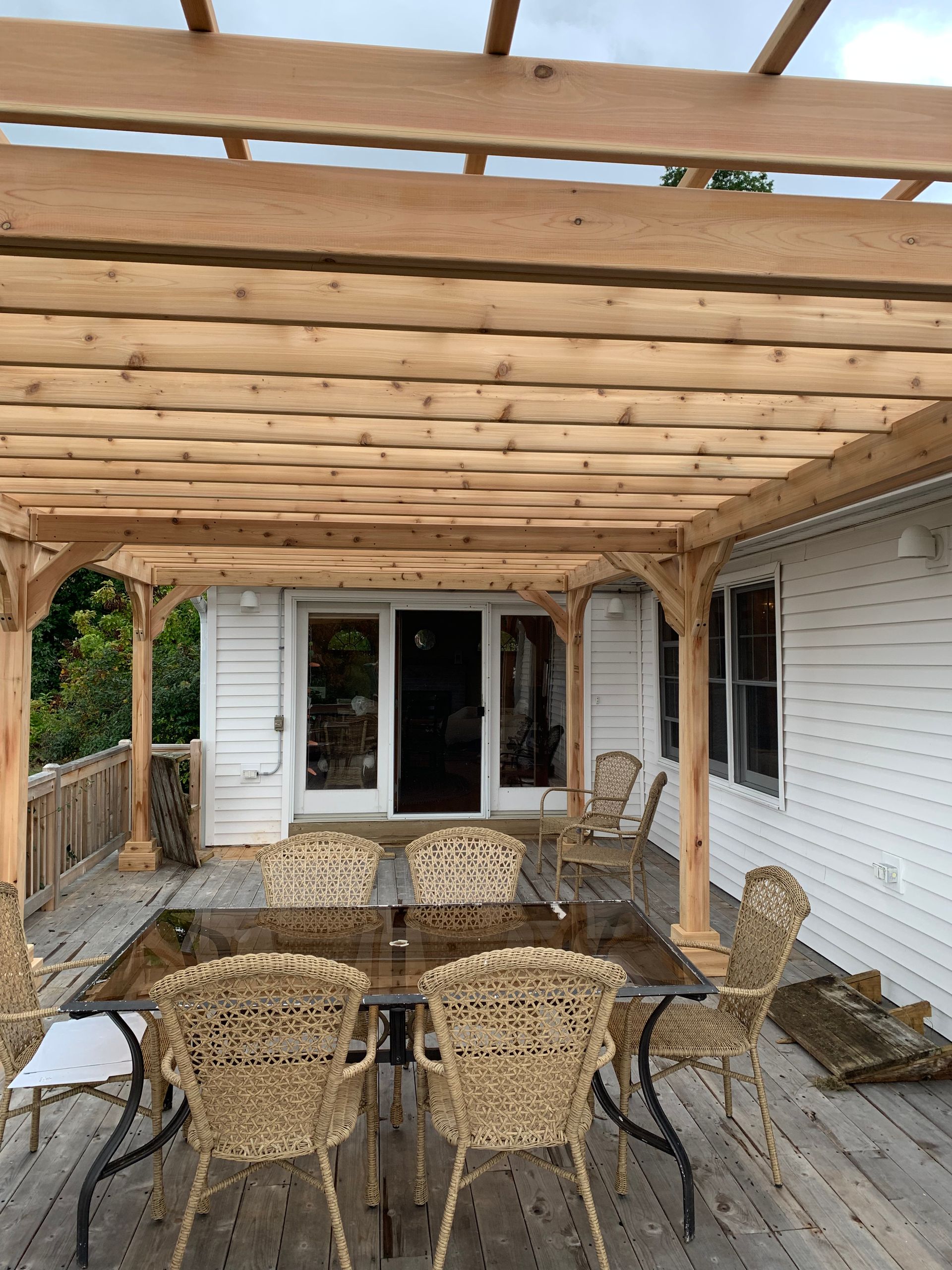 Covered backyard patio with wicker chairs, outdoor table, and wooden pergola ceiling