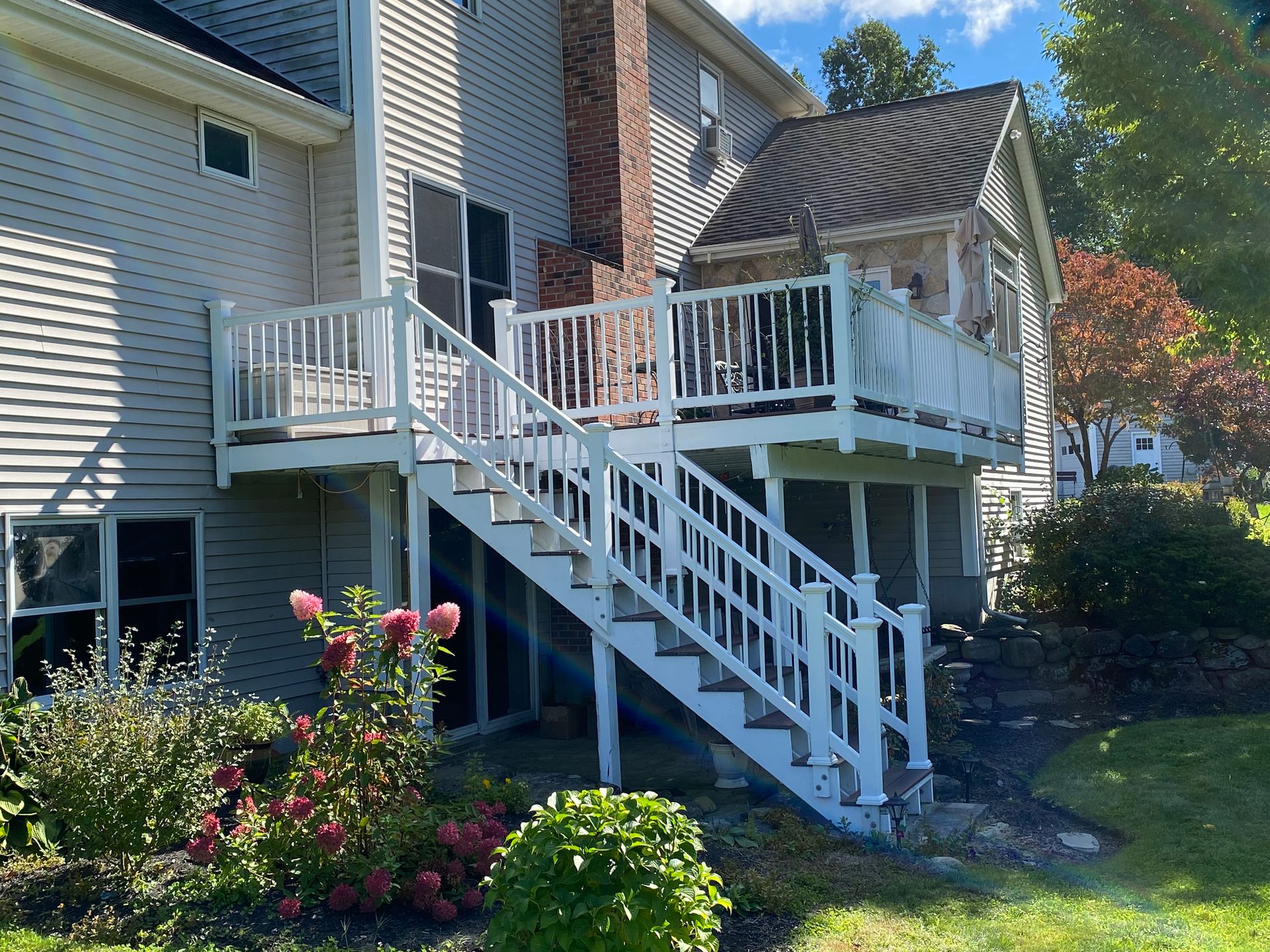 Backyard deck with white stairs, railing, and flowering garden beside a house