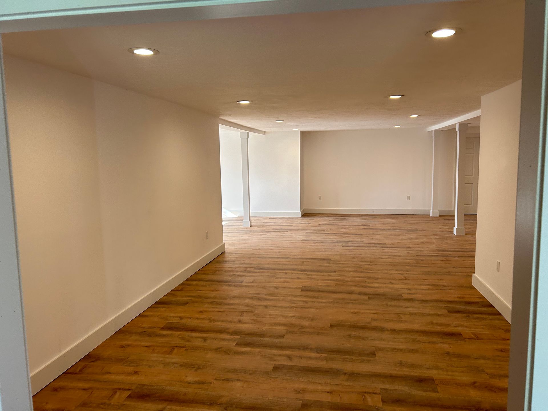 Empty modern room with wood floors, white walls, and recessed ceiling lights