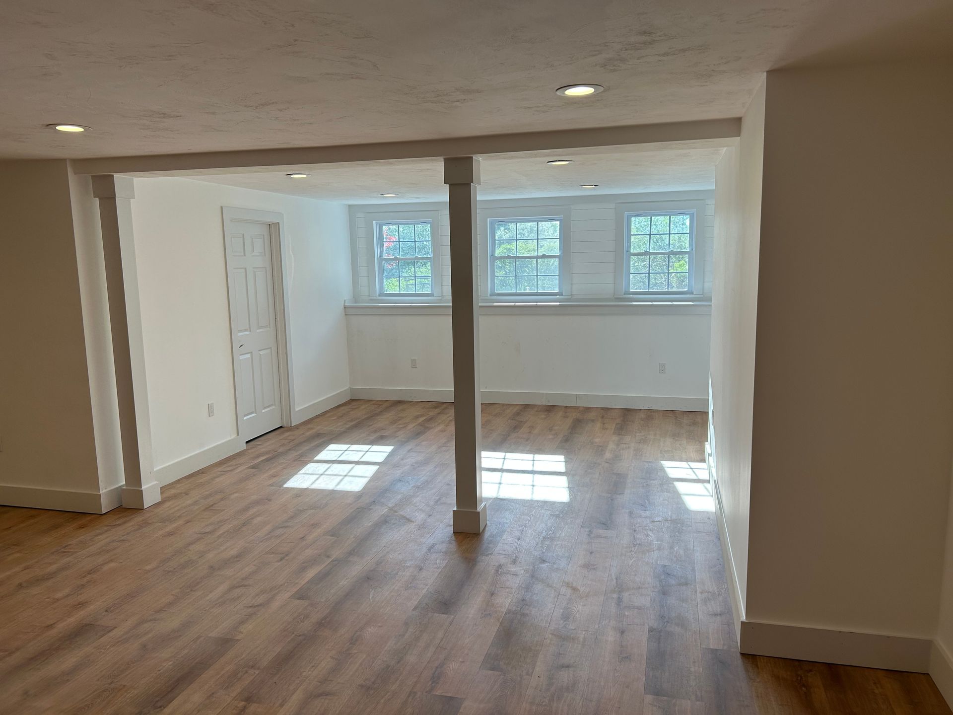 Empty living room with wood floors, white walls, and sunlight streaming through three windows.