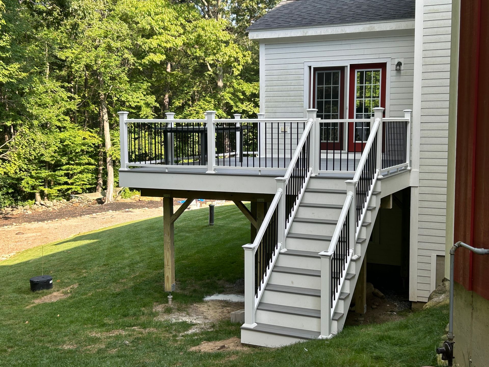 House deck with stairs and black railing beside a red shed, set in a grassy yard.