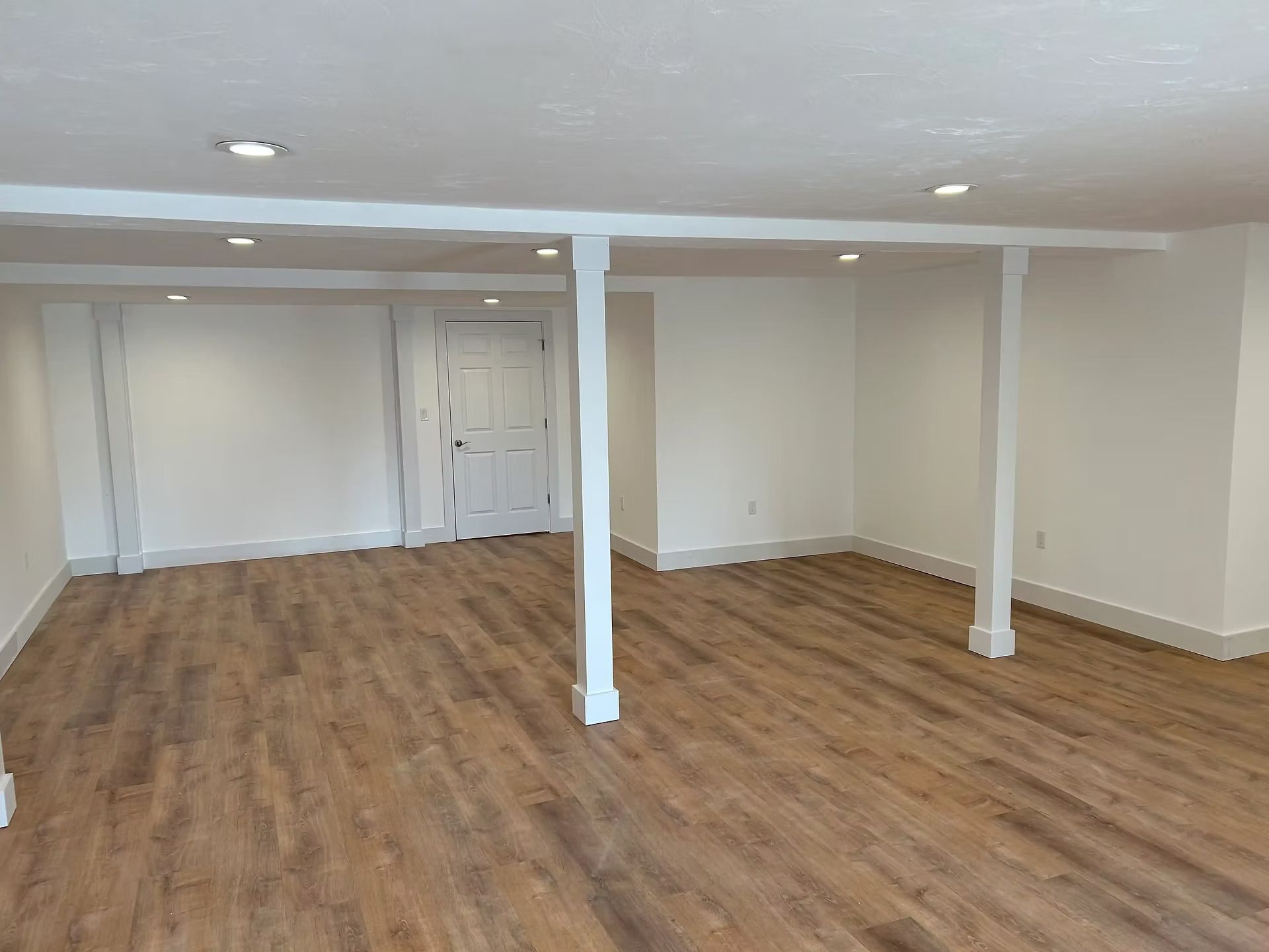 Empty beige room with wood-look flooring, white columns, and recessed ceiling lights